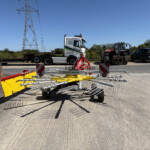 White truck with 'RUSSELLS' branding parked on a road beside heavy machinery, power pylons in the background under a clear blue sky.
