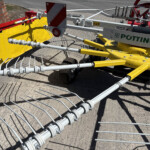 Close-up of a roadwork barrier with yellow fabric, red reflector, and multiple steel arms.