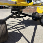 Close-up of a yellow industrial frame with metal support arms and black wheels on a concrete surface, likely part of an agricultural sprayer.