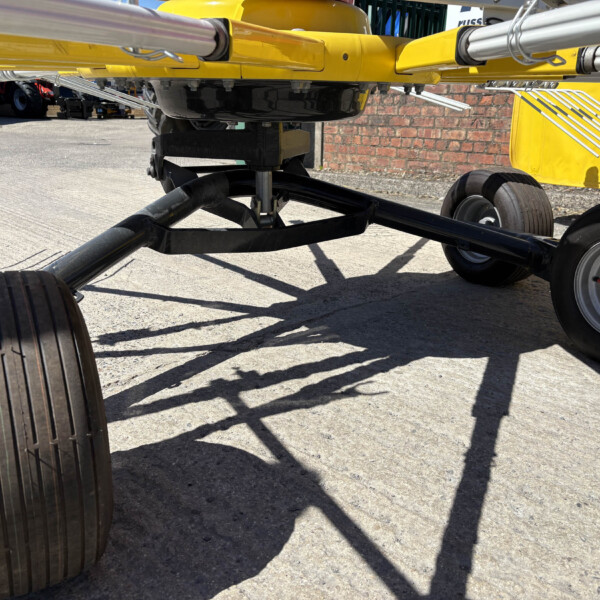 Close-up of a yellow industrial frame with metal support arms and black wheels on a concrete surface, likely part of an agricultural sprayer.