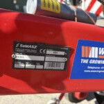 Close-up of a red industrial machine showing a metal data plate with model/serial information and a blue 'Weaving Machinery' sticker nearby.