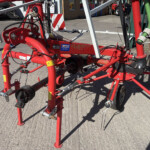 Close-up of red farming equipment frame with hydraulic hoses and metal bars on a concrete yard.