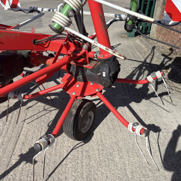 Close-up of a red farming implement with sharpened tines on a concrete surface.