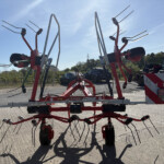 Red farming implement with multiple tines mounted on a trailer in a sunny outdoor yard