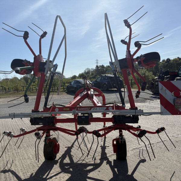 Red farming implement with multiple tines mounted on a trailer in a sunny outdoor yard