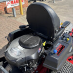 Close-up of a ride-on lawn mower with a black seat, dashboard controls, and large treaded rear wheels at a dealership lot. The Kohler 7000 Series badge is visible on the front.