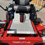 Rear view of a red TimeCutter ride-on mower showing the gray/black cushioned seat, yellow coil spring suspension, and diamond-plate foot deck.