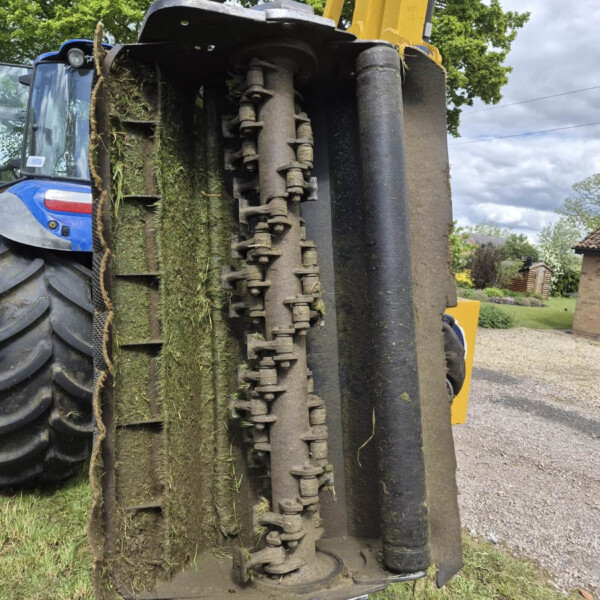 Close-up of a muddy excavator track and hydraulic components, with a yellow boom visible on a grassy site.