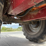Underbelly of a red agricultural machine showing large tire, metal frame, and hoses with dirt and wear visible