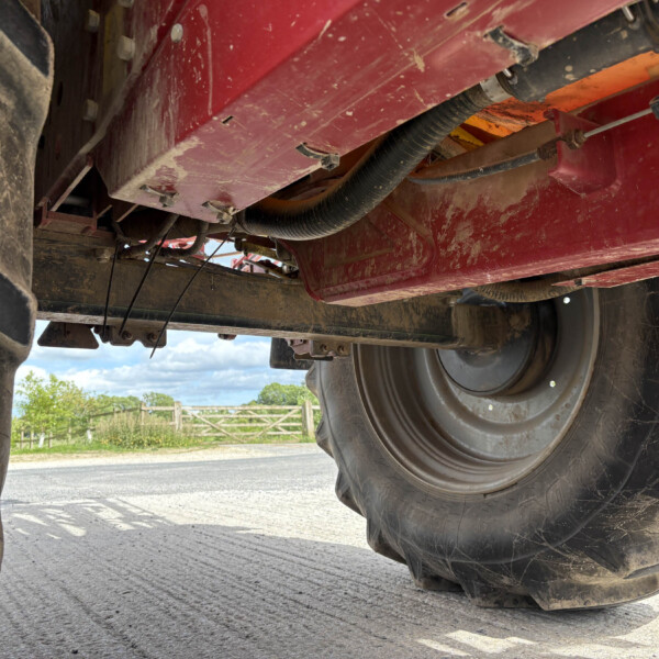 Underbelly of a red agricultural machine showing large tire, metal frame, and hoses with dirt and wear visible