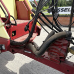 Close-up of hydraulic hoses and red metal frame on an industrial machine outdoors.