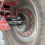 Close-up of a red agricultural machine’s wheel hub with red spoke ring, black central hub, and dusty metal components visible beside a muddy tire edge.