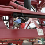 Close-up of red metal framework with exposed hydraulic hoses, connectors and wiring on agricultural equipment on a sunny day