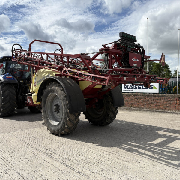 Red agricultural sprayer equipment mounted on a tractor, on display outdoors at a dealership.