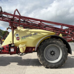 Red agricultural sprayer frame with a yellow Navigator 3000 tank, hoses and controls, parked on pavement under a cloudy sky.