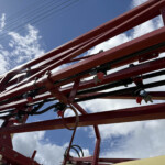 Red metal framework of a ride structure against a blue sky with clouds, viewed from below.