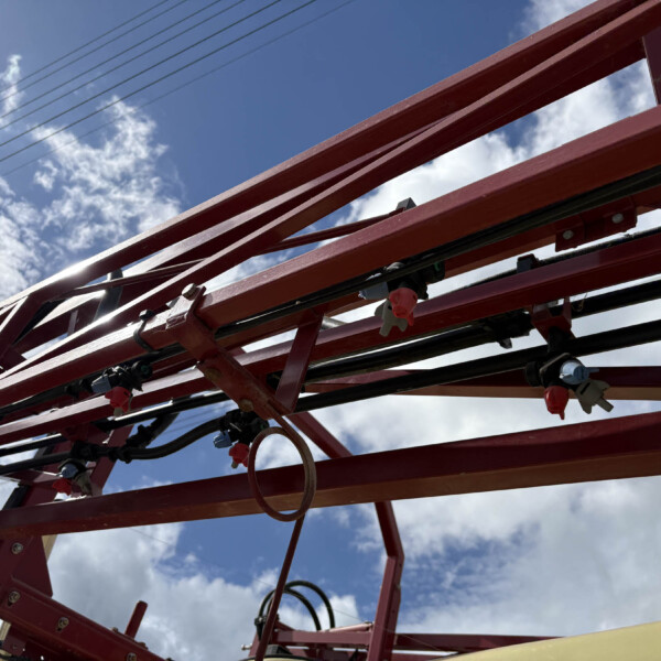 Red metal framework of a ride structure against a blue sky with clouds, viewed from below.
