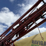 Close-up of red metal support beams with cables and bolts against a blue sky, part of an amusement ride frame seen from below.