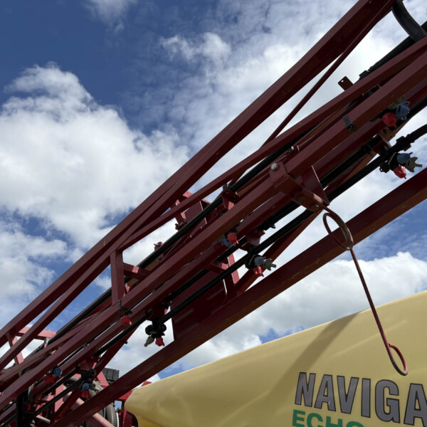 Close-up of red metal support beams with cables and bolts against a blue sky, part of an amusement ride frame seen from below.