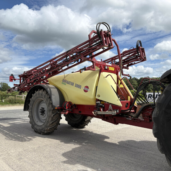 Red agricultural sprayer with a yellow tank labeled Navigator 3000, mounted on large wheels in a parking area.