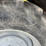 Close-up of a dusty tire and grey wheel rim, showing dirt, scratches, and mud on the surface.
