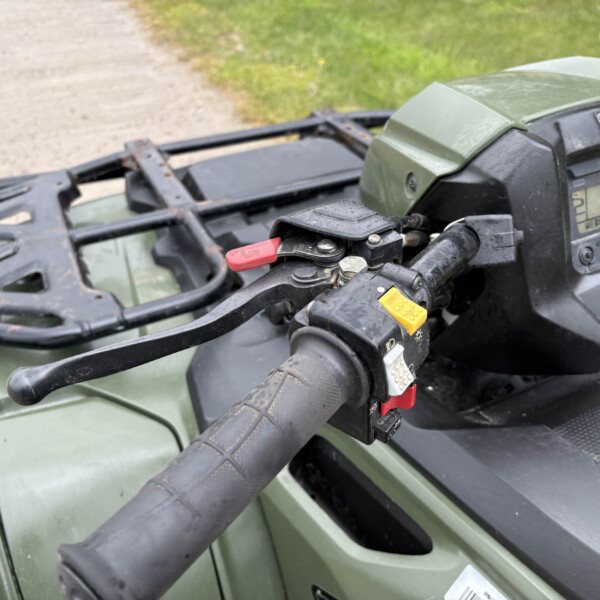 Close-up of a green ATV cockpit showing handlebars, red ignition/kill switch, and a digital gauge reading 0.