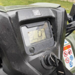 Close-up of a dusty black motorcycle dashboard with a Honda emblem and a digital speedometer reading 0 km/h.