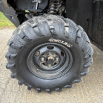 Close-up of a large muddy off-road tire with deep knobby tread on a utility vehicle