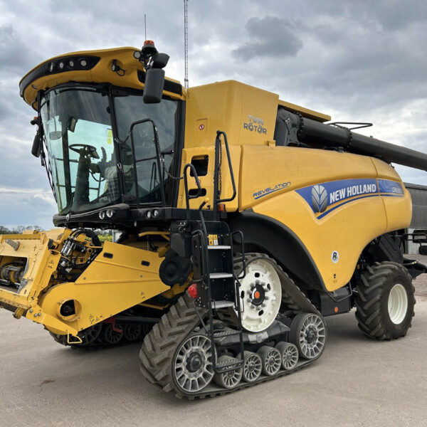 Yellow New Holland combine harvester with multi-row caterpillar tracks parked on a concrete surface; cloudy sky above.