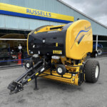 Yellow New Holland agricultural header on a tractor-like machine displayed outside the Russells store, with a large tire visible in the foreground.