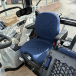 Interior view of a vehicle cab with a blue driver's seat, surrounded by plastic sheeting and a cardboard box on a surface near the window.