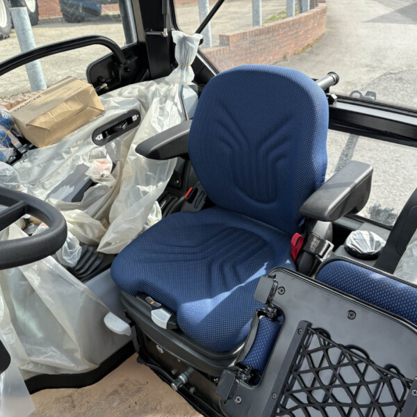 Interior view of a vehicle cab with a blue driver's seat, surrounded by plastic sheeting and a cardboard box on a surface near the window.