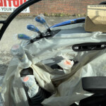 Car interior covered in protective plastic wrap, with blue wrapped components and a cardboard box resting on the seat.