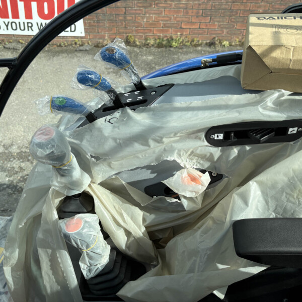 Car interior covered in protective plastic wrap, with blue wrapped components and a cardboard box resting on the seat.
