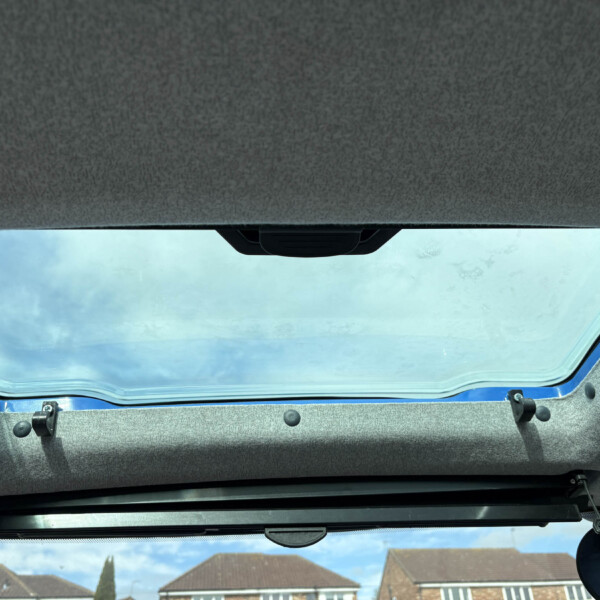 Open car sunroof view: blue sky and rooftops seen through the roof opening from inside the vehicle