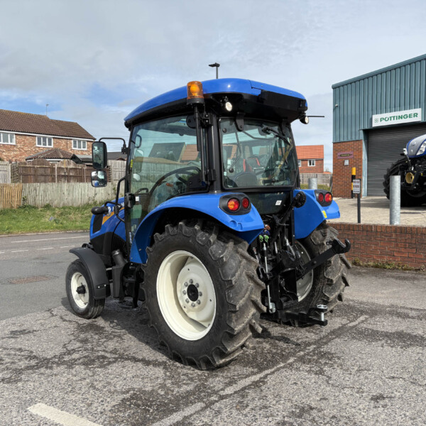 Blue tractor in a parking lot near a POTTINGER building; large rear wheel in the foreground.