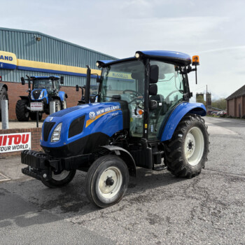 Blue New Holland tractors parked outside a dealership building with yellow-and-blue signage reading 'NEW HOLLAND'.