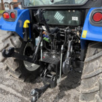 Rear of a blue tractor showing the hitch, hydraulic hoses, and large rugged tires on a paved surface