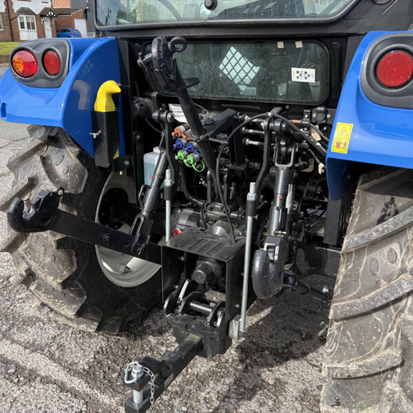 Rear of a blue tractor showing the hitch, hydraulic hoses, and large rugged tires on a paved surface