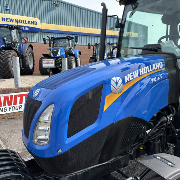 Blue New Holland tractors lined up outside a dealership; the sign reads NEW HOLLAND.