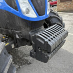 Front close-up of a blue tractor showing the headlight, grille, and heavy black steps.