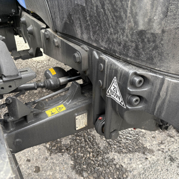 Close-up of a heavy-duty trailer chassis with bolts, brackets, and hoses amid a mesh panel and dark metal frames.