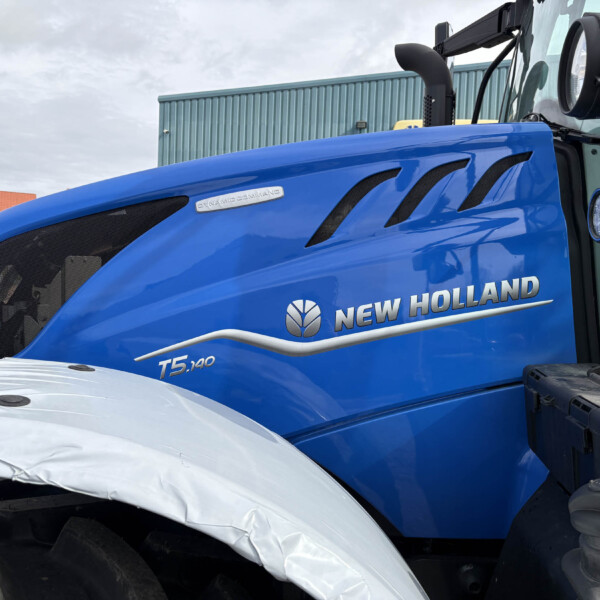 Close-up of a blue New Holland T5.140 tractor hood, showing black vent slots and a 'Dynamic Command' badge along the side.