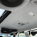 Interior of a vehicle ceiling with an overhead control panel, sunroof opening and dome light.",