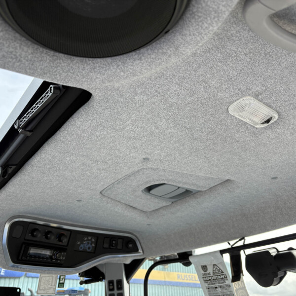 Interior of a vehicle ceiling with an overhead control panel, sunroof opening and dome light.",