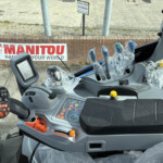 Inside a Manitou forklift cab: plastic-wrapped joysticks, control panel, and display monitor