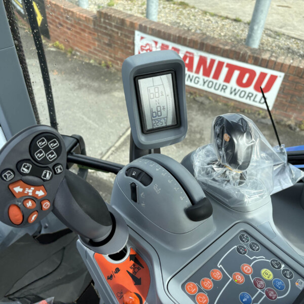 Close-up of a tractor/CNH-style cockpit: joystick with numerous orange buttons, a covered lever, and a nearby control panel inside the cabin.