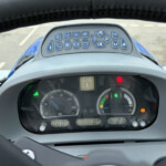 Close-up of a tractor cockpit dashboard with blue control buttons arranged above the gauge cluster and steering wheel in the foreground.