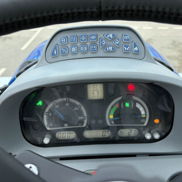 Close-up of a tractor cockpit dashboard with blue control buttons arranged above the gauge cluster and steering wheel in the foreground.