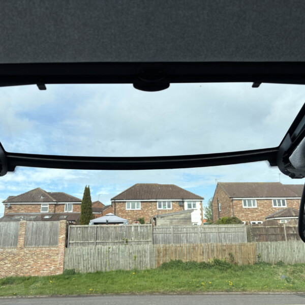 Inside a car with the sunroof open, looking out at a suburban neighborhood with brick houses and a wooden fence.